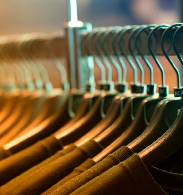 A row of neatly arranged clothes hanging on a rack with wooden hangers.
