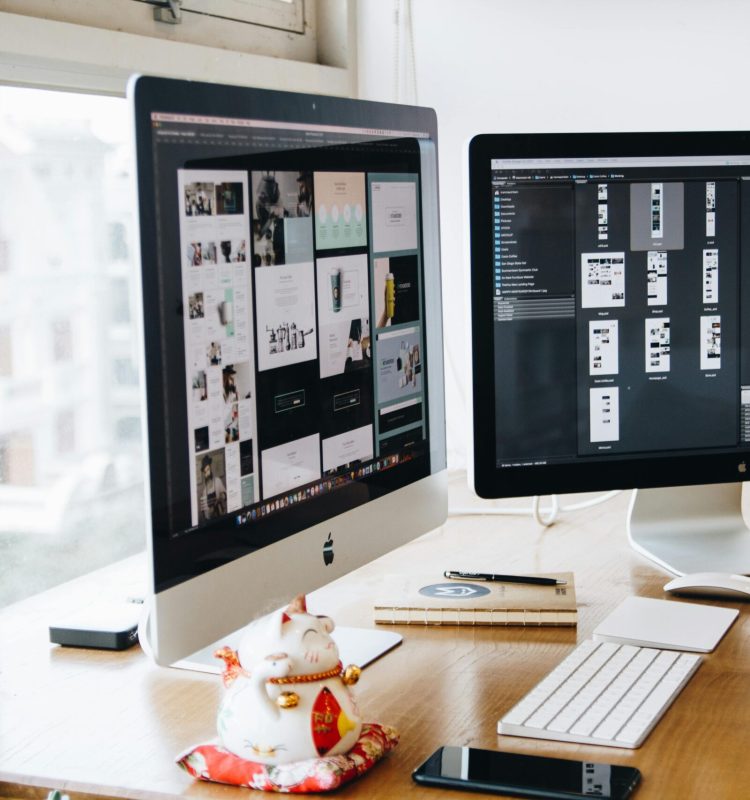 A sleek modern office setup featuring dual monitors, Apple devices, and creative decor in an indoor workspace.